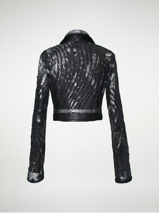 A back view of a black and silver distressed cotton waist-length jacket with overlays of sequins, black lace, metallic embossed leather, and black leather.