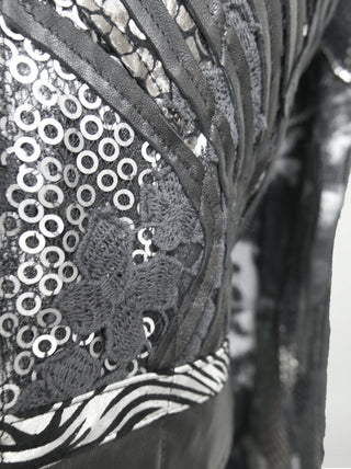 A closeup of a black and silver distressed cotton waist-length jacket with overlays of sequins, black lace, metallic embossed leather, and black leather.