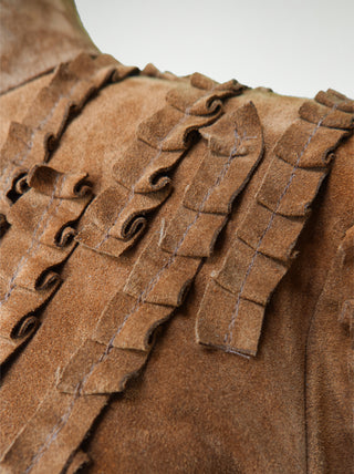 A closeup of a brown suede over-bust shrug jacket with long sleeves and strips of pleated leather stitched onto the shoulders and sleeves.