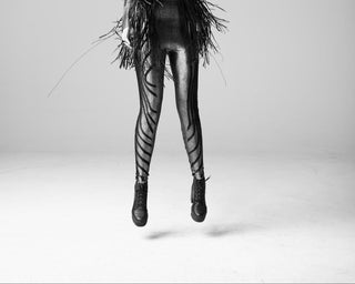 Person wearing a black leather outfit with fringed accents on a gray background