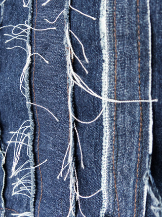 A closeup of a women's blue denim over-bust shrug with long sleeves and raw edge patchwork.