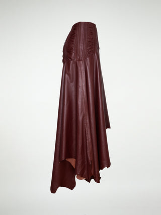 A side view of a maxi-skirt with an asymmetrical hemline, made of oxblood leather, featuring a metal zipper closure at the back.