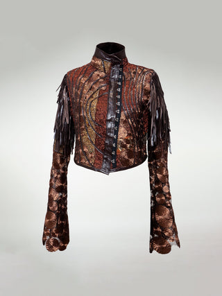 A copper and brunt orange gathered mosaic jacket with bronze lace sleeves, leather fringes on the shoulders, leather appliqué on the body, and an asymmetrical hook and eye closure.
