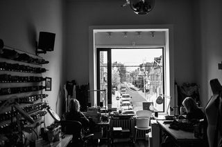 Two people sitting in the Call and Response toronto studio in black and white. Sewing machines, thread walls, and a cutting board can be seen.