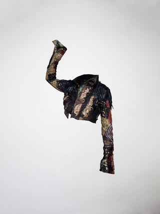 A 3/4 view of a cropped black, gold, and red mosaic jacket. Featuring leather fringes, french lace, antique tapestry, and embossed leather appliqué.