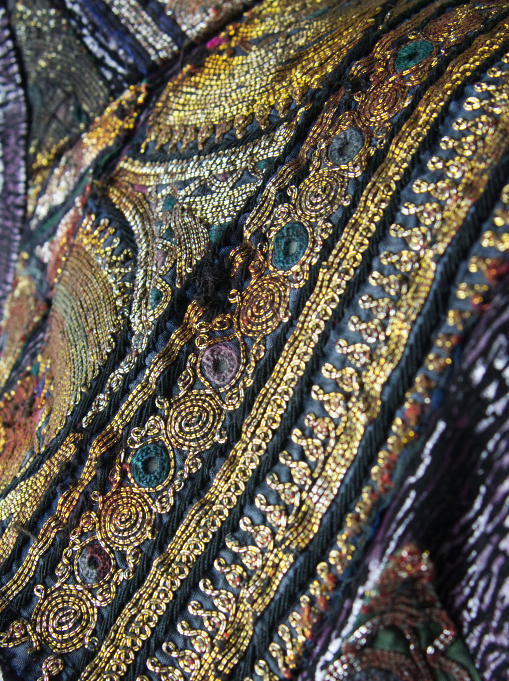 A close-up view of an over-bust shrug that is encrusted with gold embroidery, mirrors, and silver threads.
