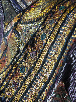 A close-up view of an over-bust shrug that is encrusted with gold embroidery, mirrors, and silver threads.