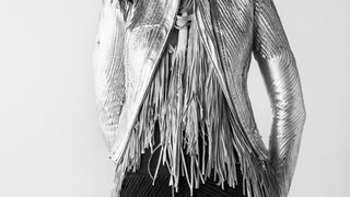 Person wearing a stylish outfit with a fringed jacket on a plain background