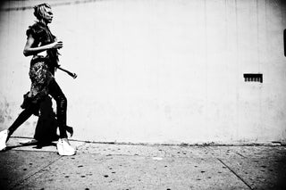Black and white photo of a person walking on a sidewalk with a plain wall in the background