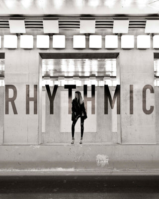Person standing in front of a wall with 'RHYTHMIC' text in a modern architectural setting.
