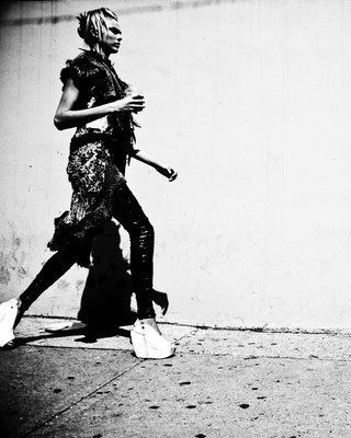 Black and white photo of a person walking on a sidewalk with a plain wall in the background