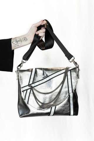 Silver handbag with black accents held by a person on a white background