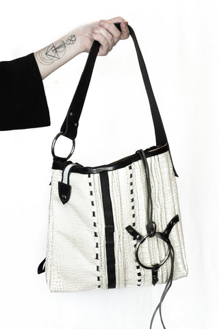 White handbag with black accents held by a person on a white background