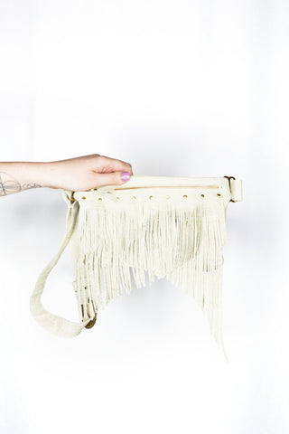 Hand holding a cream-colored handbag with fringe details against a white background