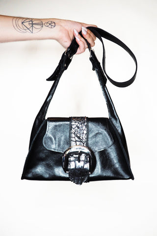 Black handbag with a silver clasp held by a person against a white background