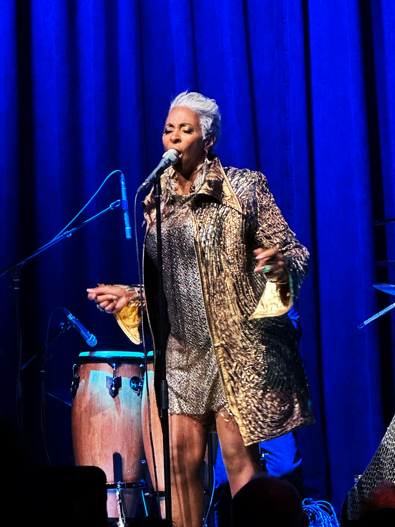 Shakura S’Aida wearing a call and response coat  and dress while performing