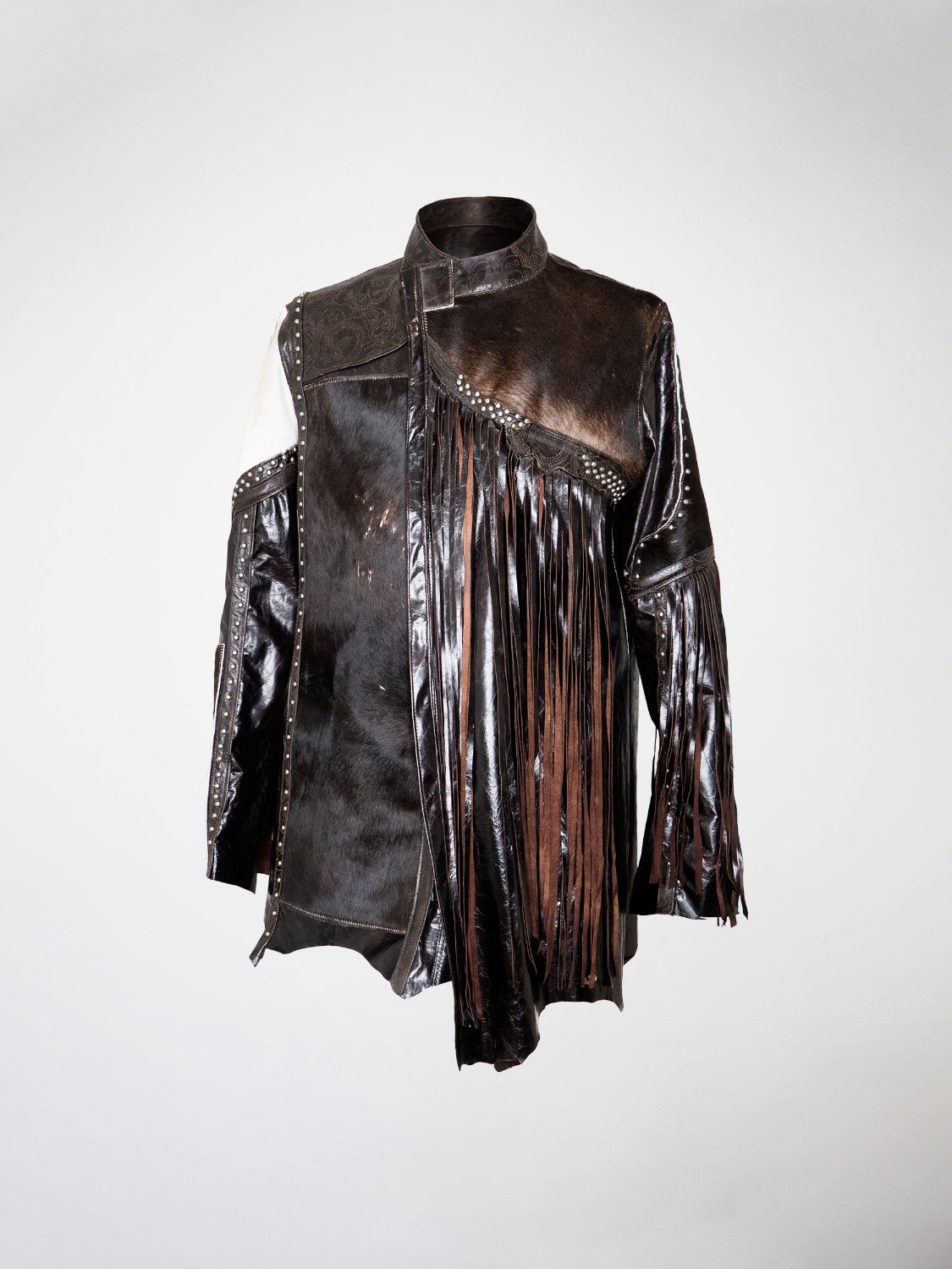 A mid-length brown leather jacket with panels of brown and white hair-on cowhide, brown embossed leather. Featuring long leather fringes on the right side and studding along seams.