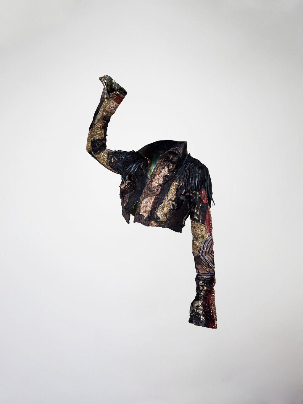 A 3/4 view of a cropped black, gold, and red mosaic jacket. Featuring leather fringes, french lace, antique tapestry, and embossed leather appliqué.