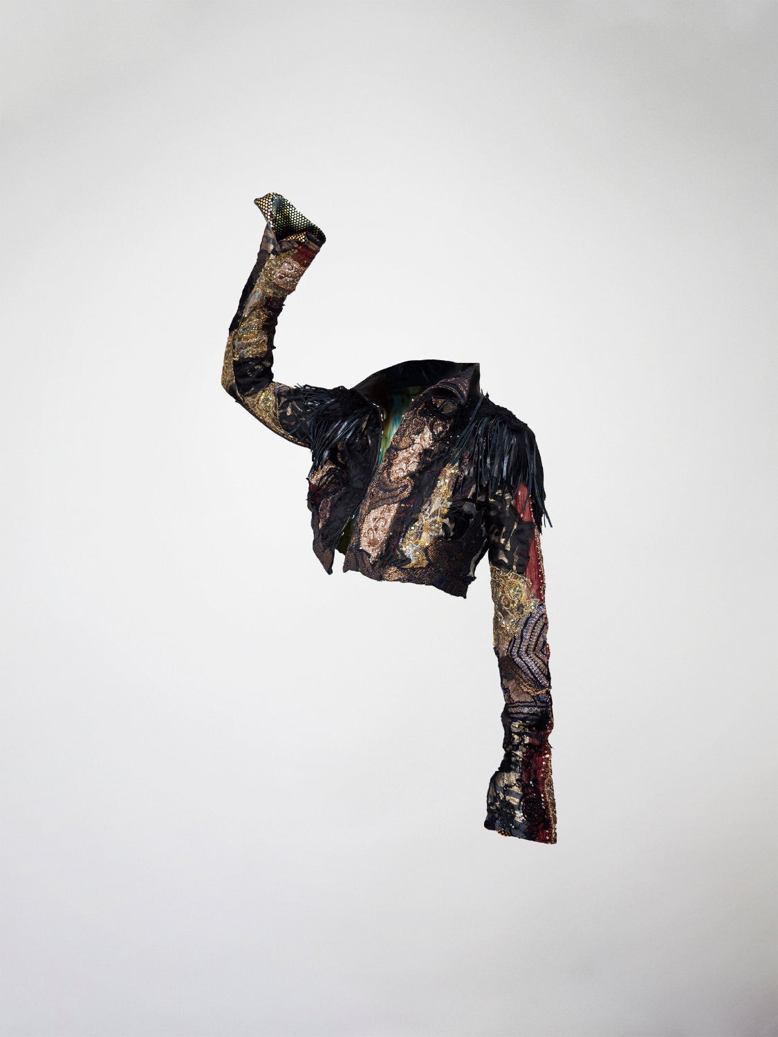 A 3/4 view of a cropped black, gold, and red mosaic jacket. Featuring leather fringes, french lace, antique tapestry, and embossed leather appliqué.