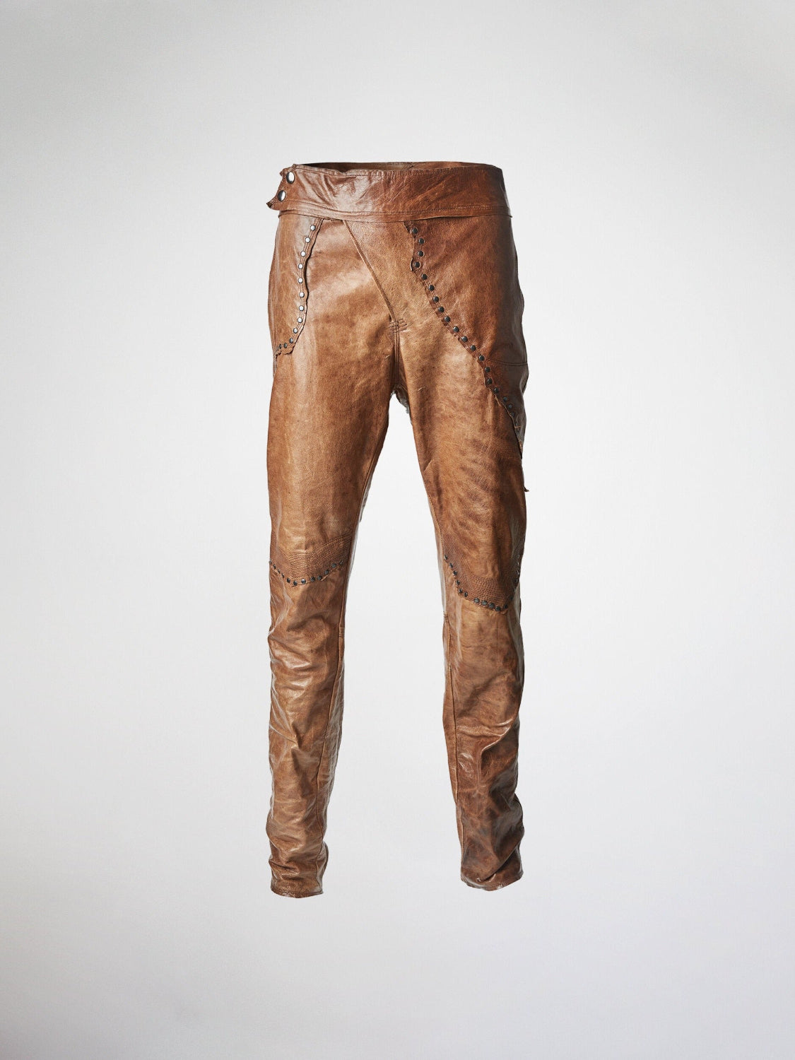 A pair of brown leather trousers with an asymmetrical fly and metal stud embellishments.